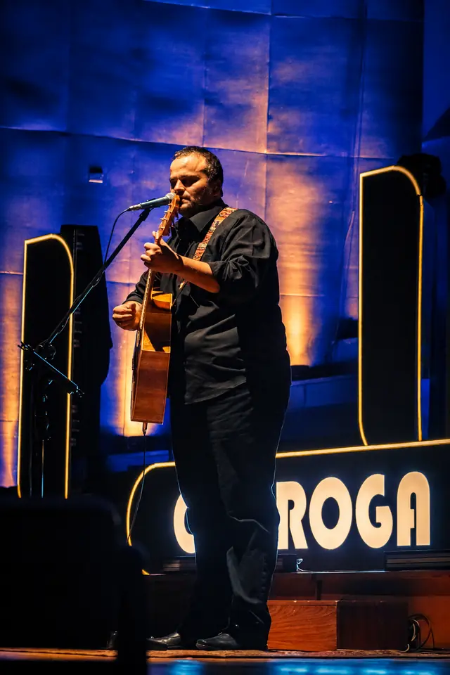 Guitarra acústica y voz frente al cartel de Cheroga
